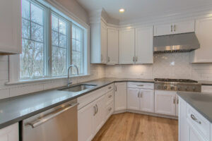 A modern kitchen with white tile backsplash, hardwood floors, white cabinets and stainless steel appliances.